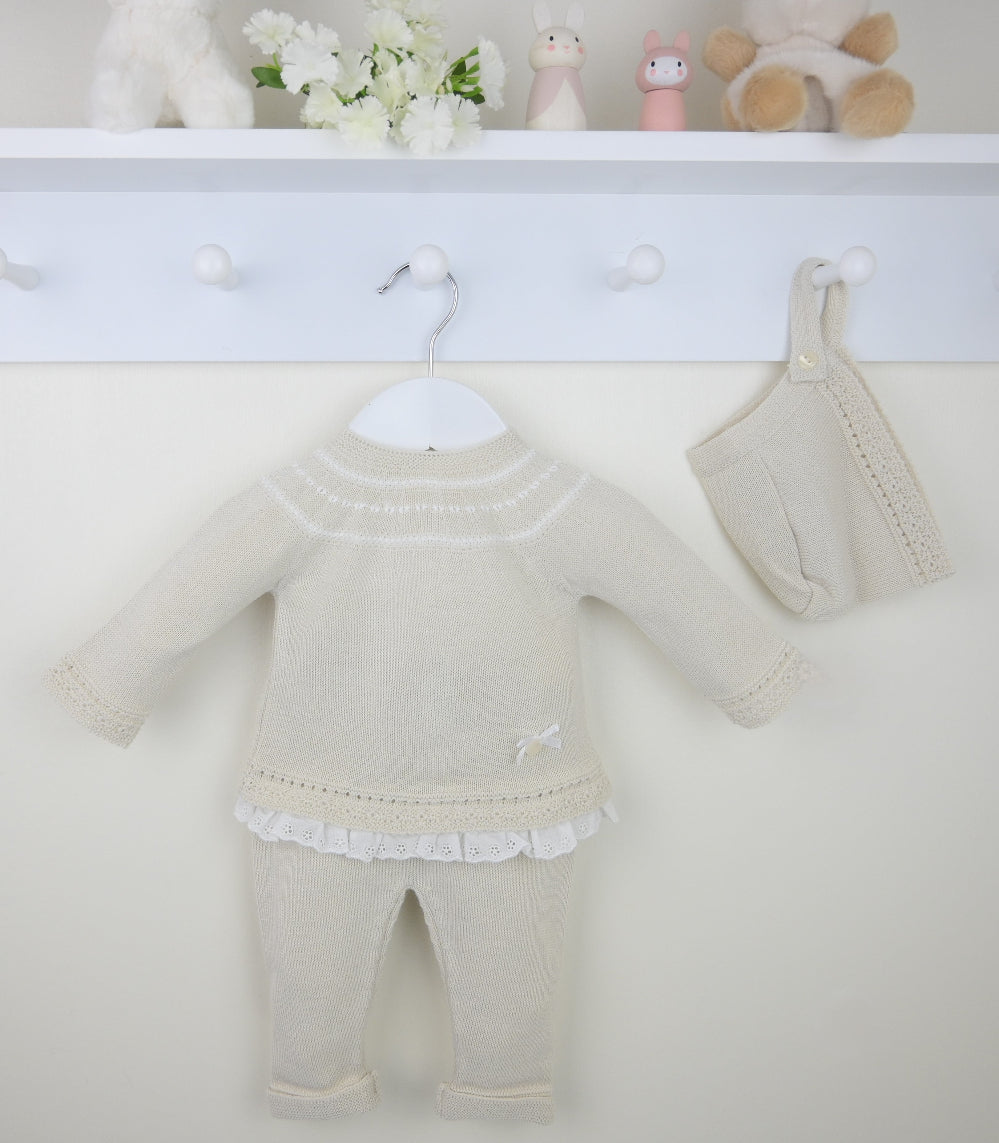 Flat lay of beige 3-piece knitted baby outfit with lace trim and bow detail