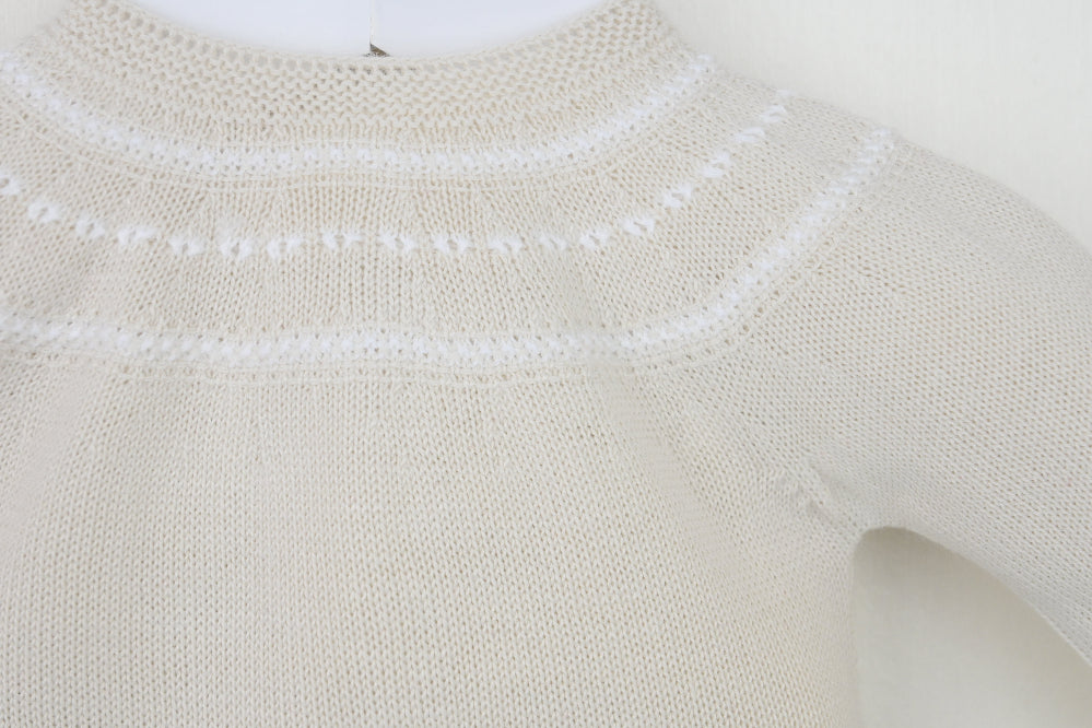 Flat lay of beige 3-piece knitted baby outfit with lace trim and bow detail