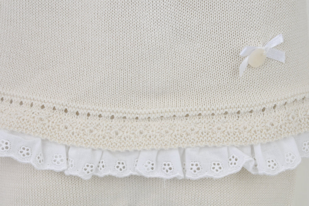 Flat lay of beige 3-piece knitted baby outfit with lace trim and bow detail