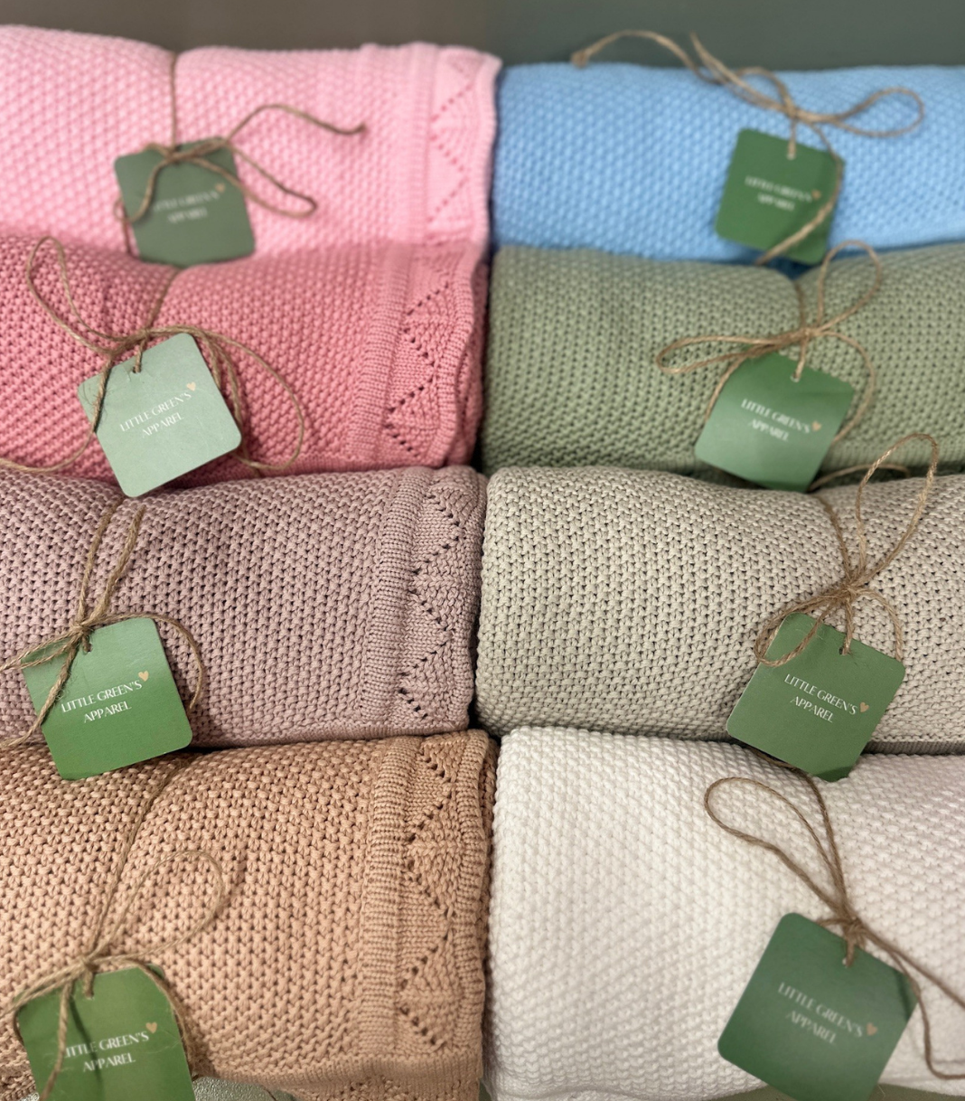 Stack of folded knitted blankets in various colors with green tags.