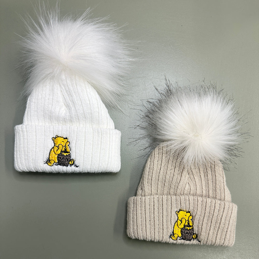 White and taupe Hunny Bear baby pom pom hats with embroidered bear motif