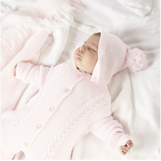 Pink knitted baby pramsuit with bobble hood by Dandelion – front view on hange