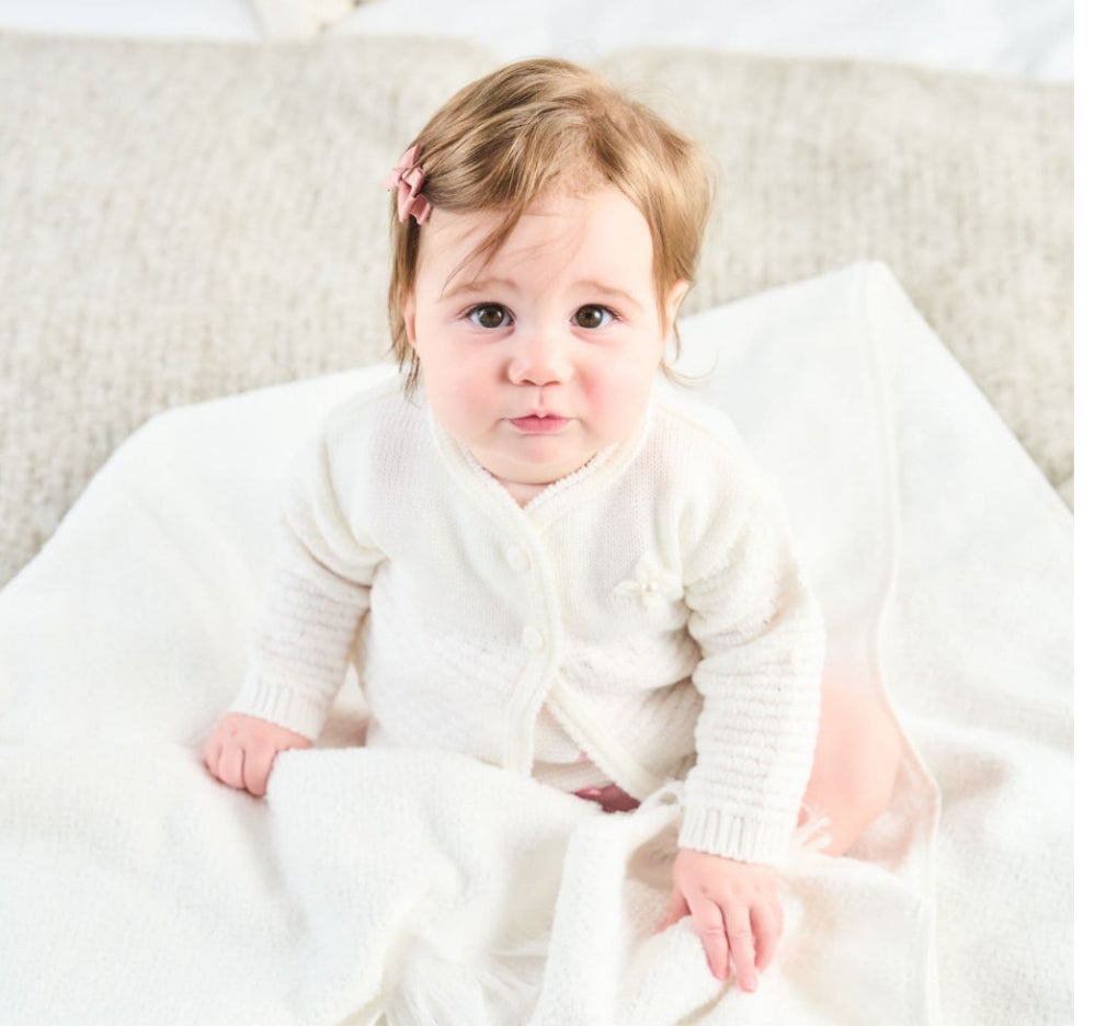Baby wearing white matinee cardigan smiling – close-up