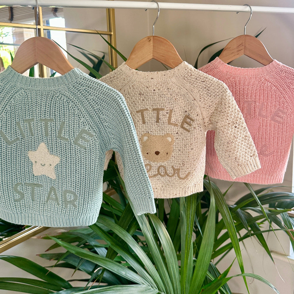 Three knitted baby cardigans in green, oatmeal fleck, and soft pink