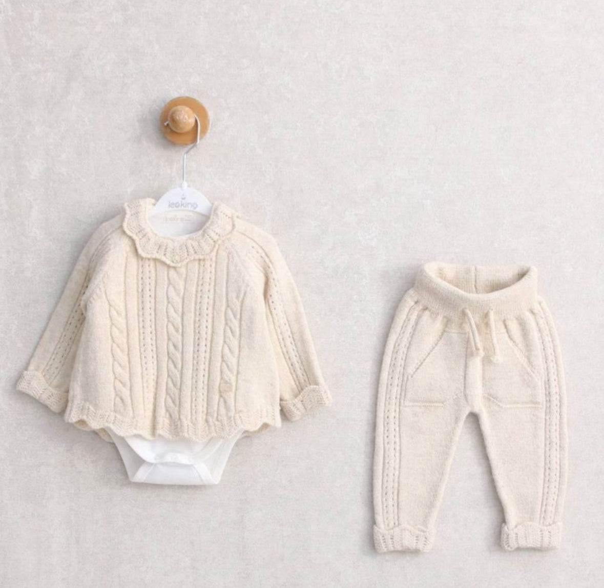 Flat lay of Leoking baby girl 3-piece knitted outfit in pink, featuring a cable-knit sweater with scalloped collar, matching joggers, and coordinating bodysuit.
