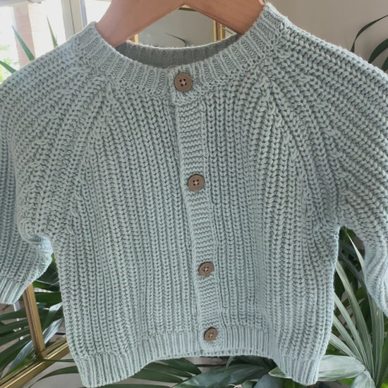 Three knitted baby cardigans in green, oatmeal fleck, and soft pink