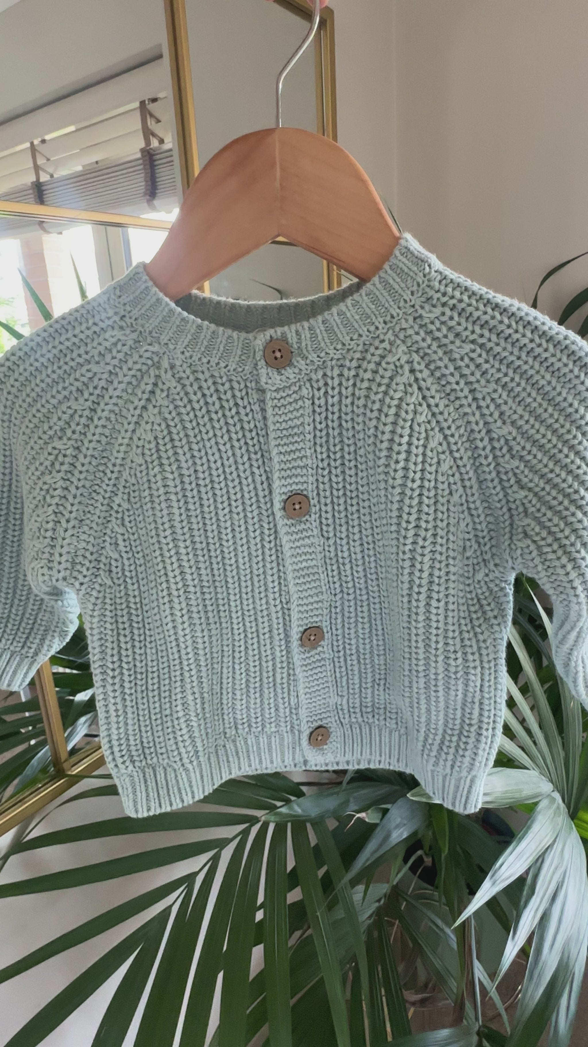 Three knitted baby cardigans in green, oatmeal fleck, and soft pink
