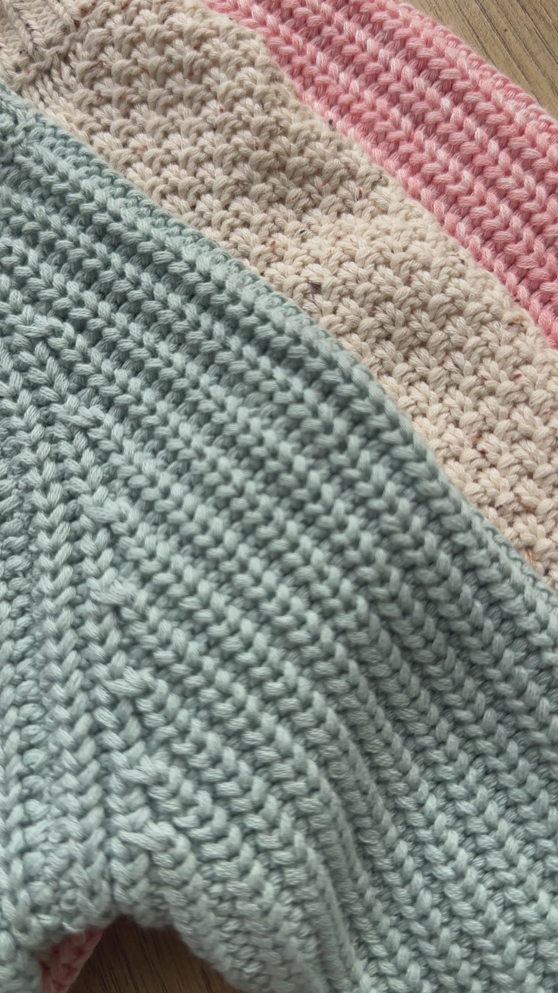 Three knitted baby cardigans in green, oatmeal fleck, and soft pink