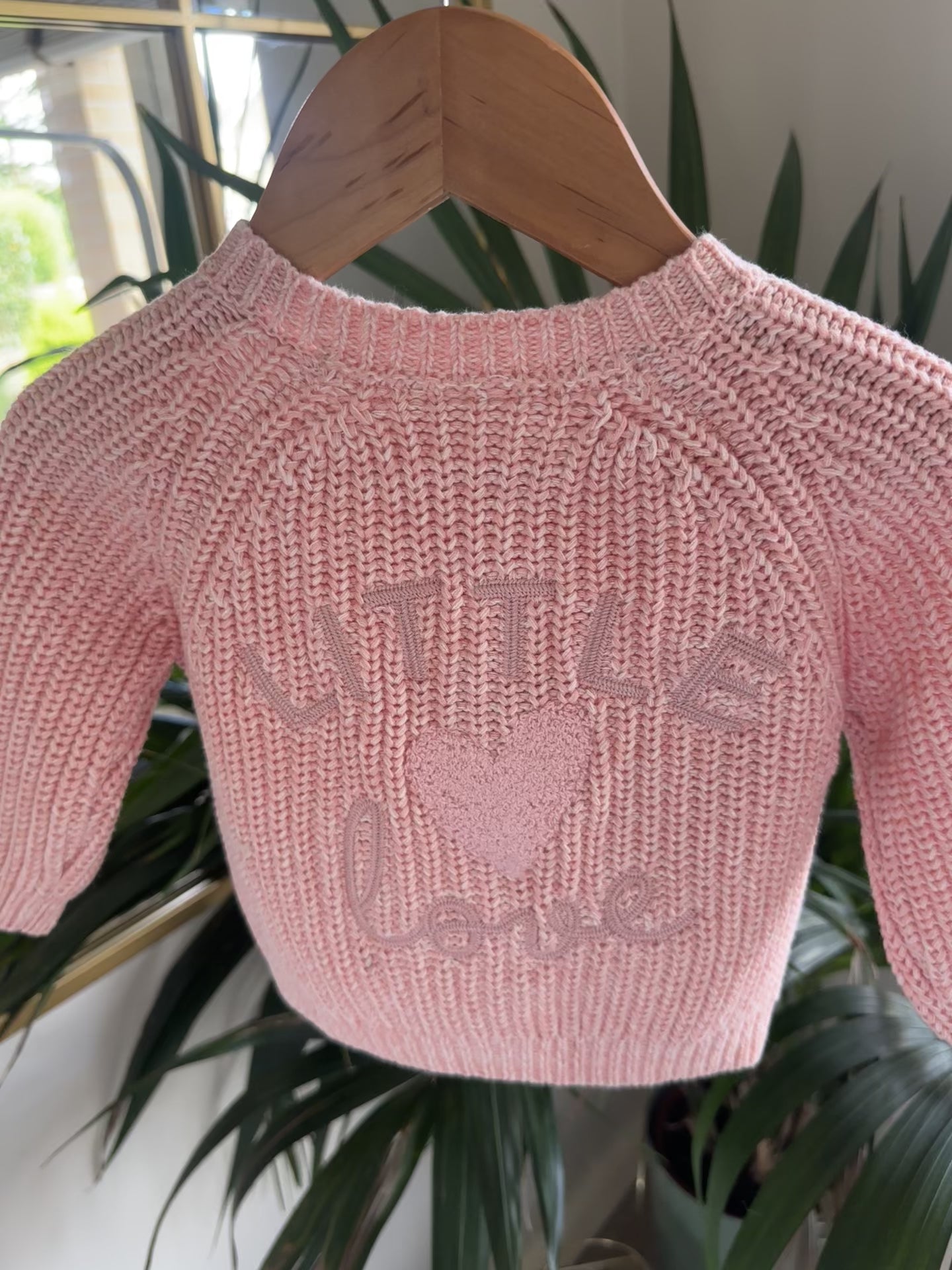Three knitted baby cardigans in green, oatmeal fleck, and soft pink