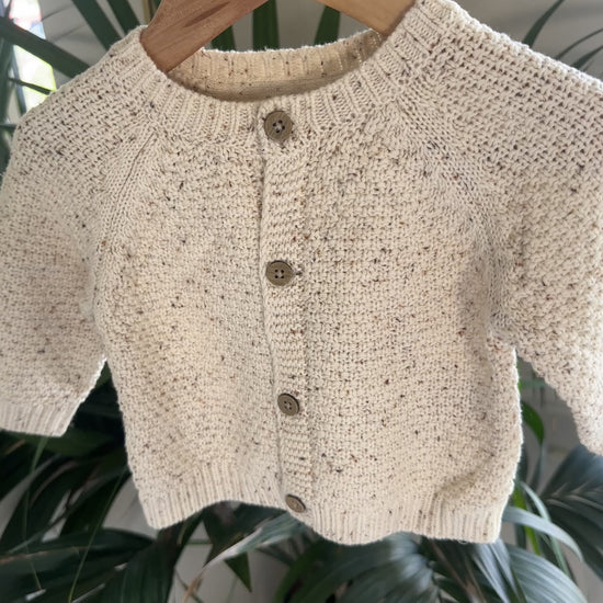Three knitted baby cardigans in green, oatmeal fleck, and soft pink