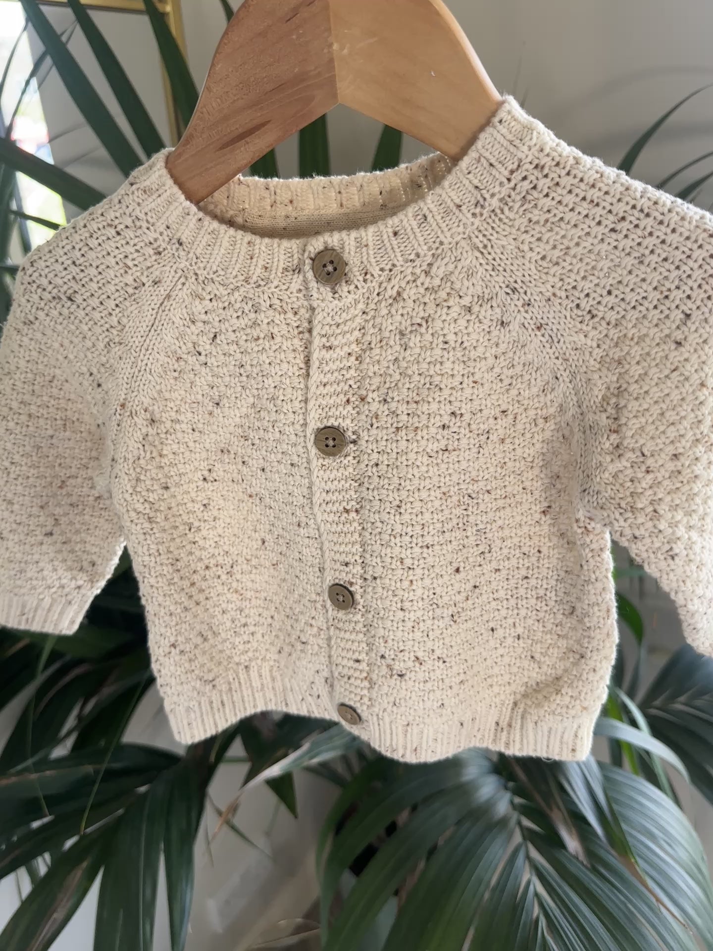 Three knitted baby cardigans in green, oatmeal fleck, and soft pink